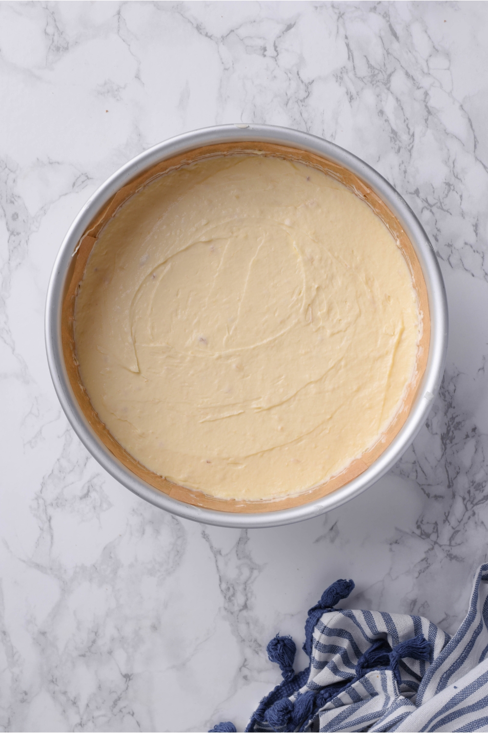 A cake pan lined with parchment paper and a layer of cheesecake spread into an even layer.