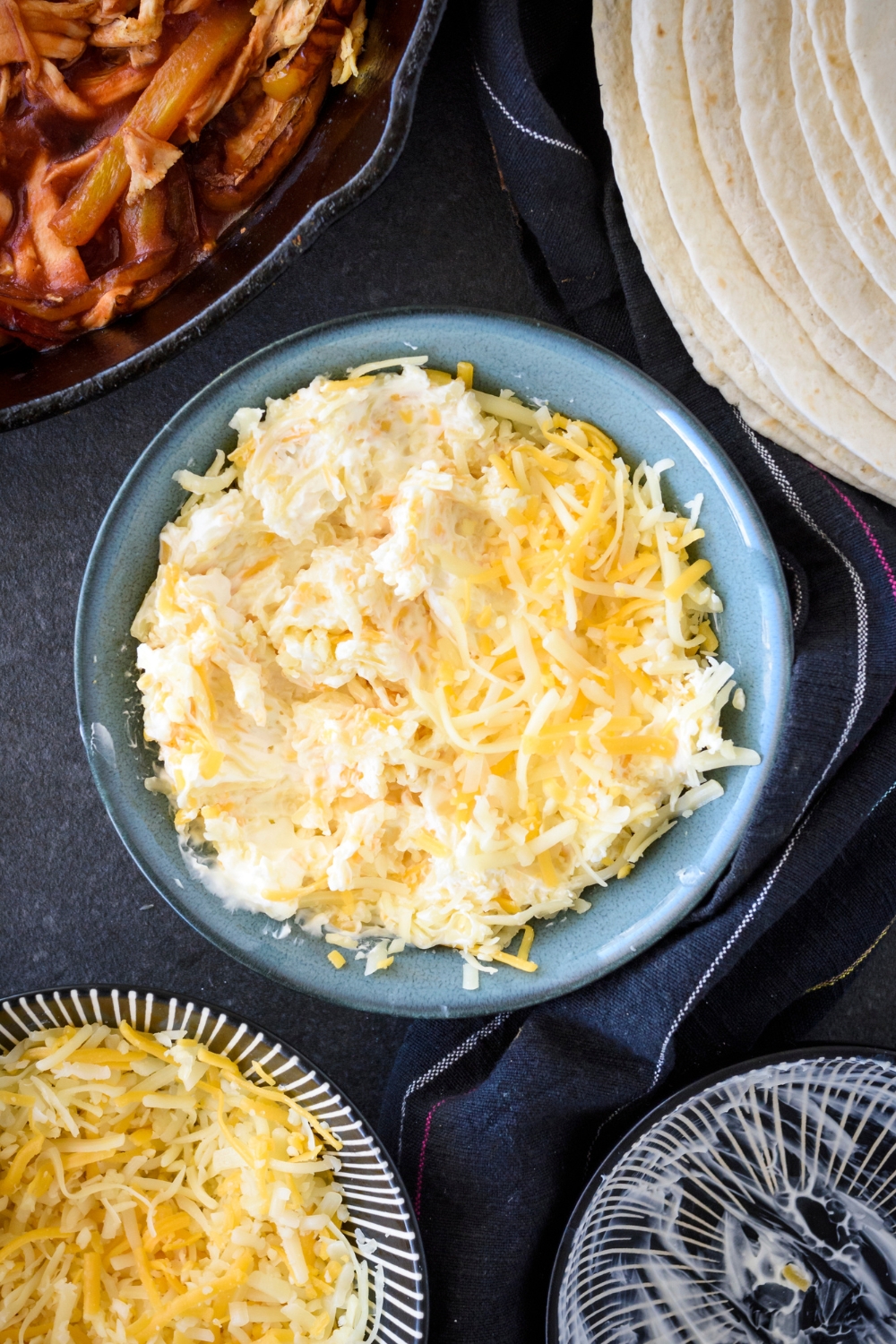 A blue bowl filled with cream cheese and shredded cheese mixed together.