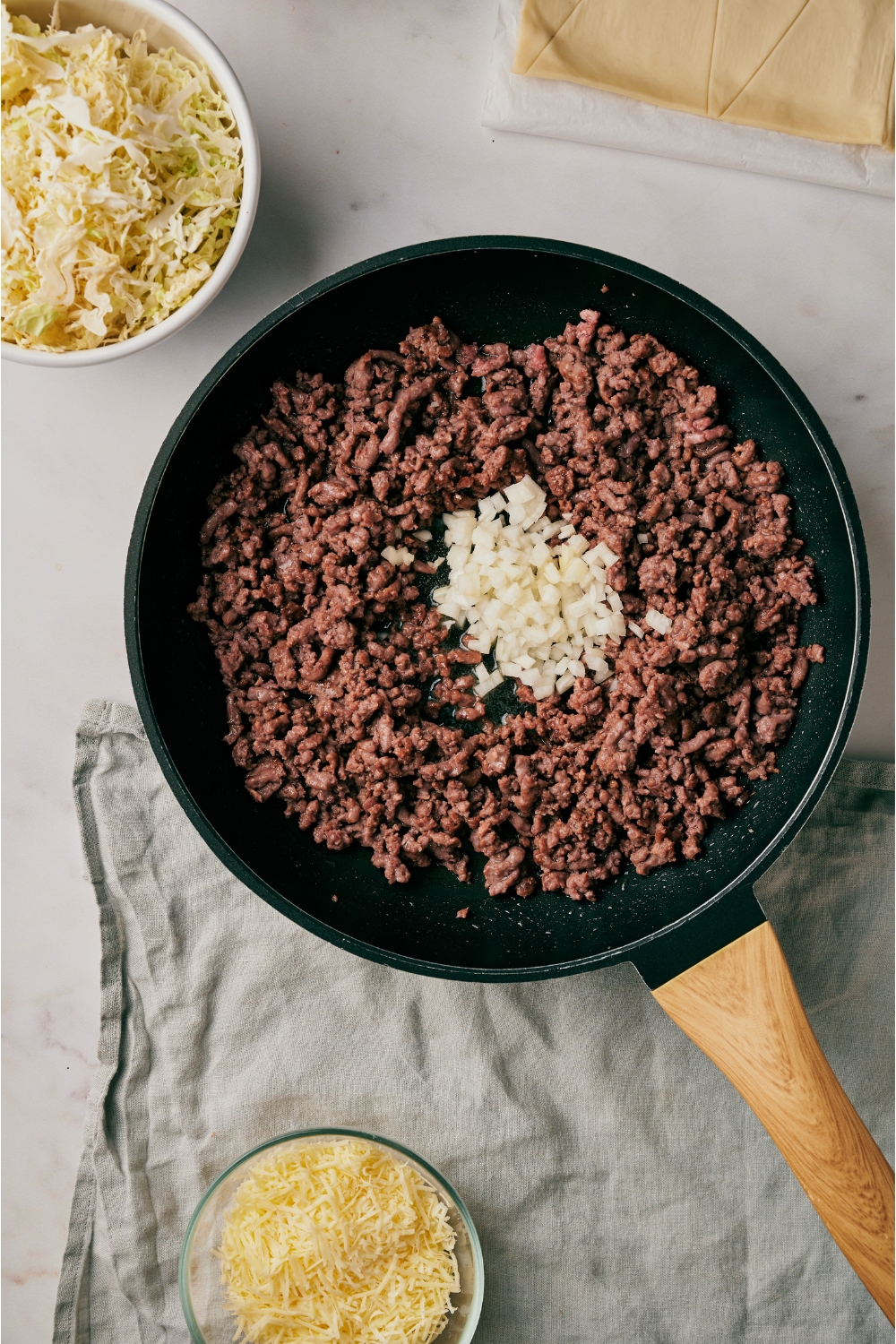 A skillet filled with ground beef and a pile of diced onions in the center.