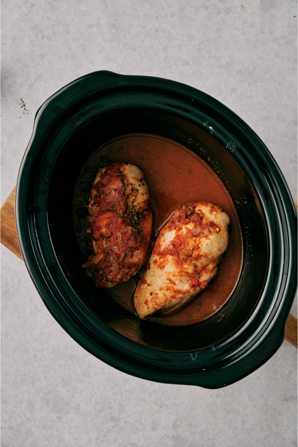 A crock pot filled with two chicken breasts covered in a red sauce.