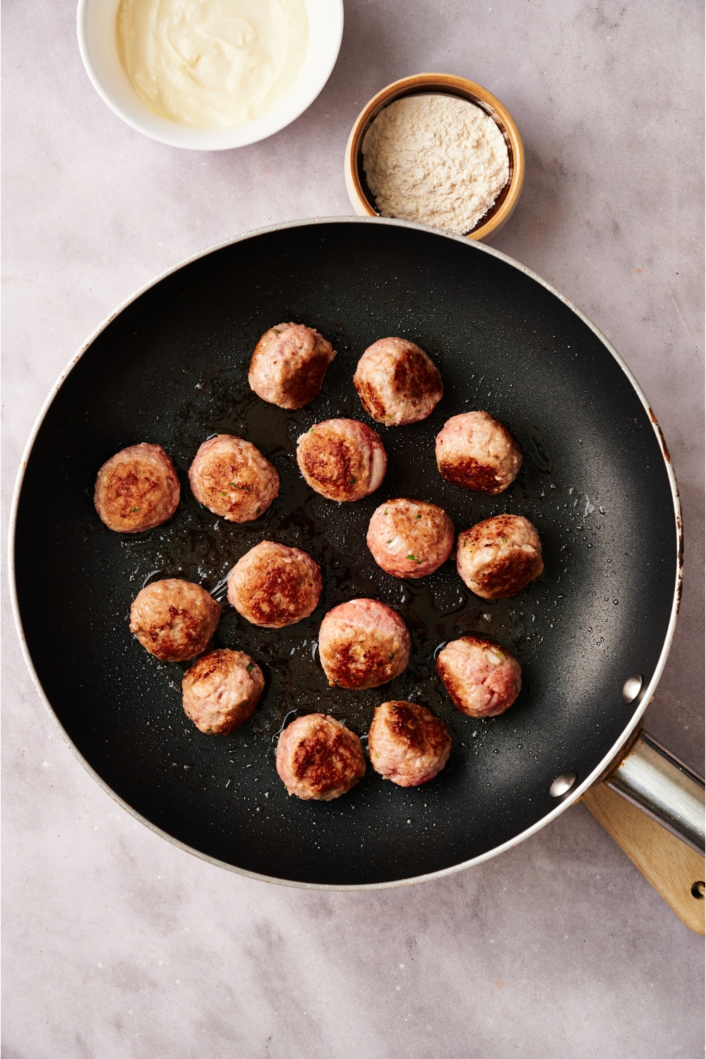A black skillet filled with meatballs cooking in oil. The meatballs are beginning to brown.