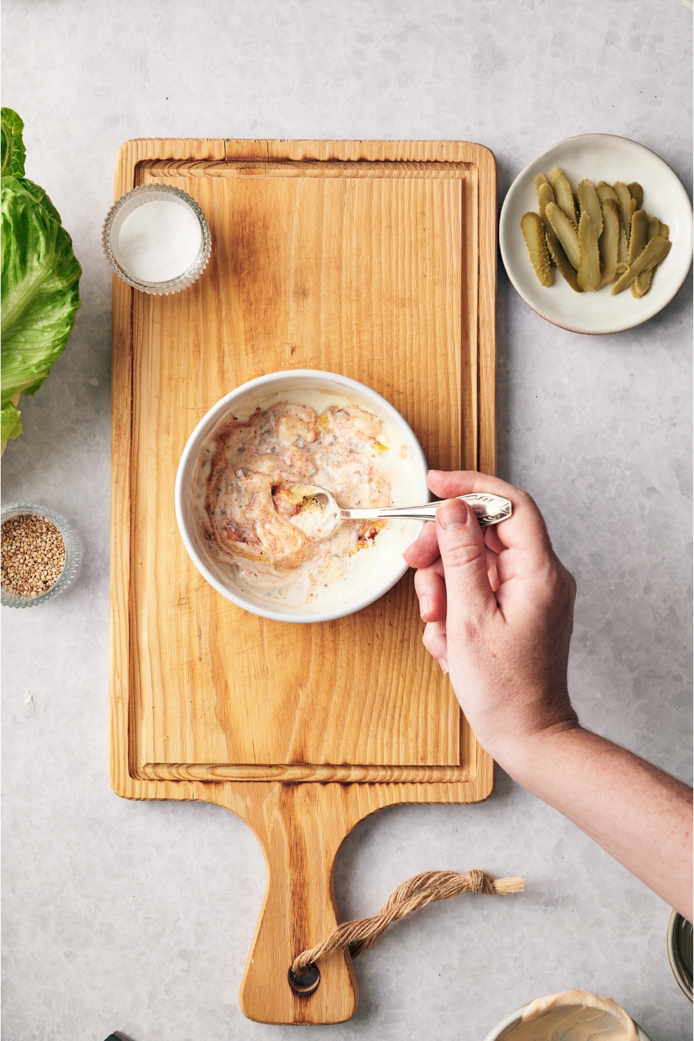 A hand using a spoon to mix sauce ingredients in a white bowl.