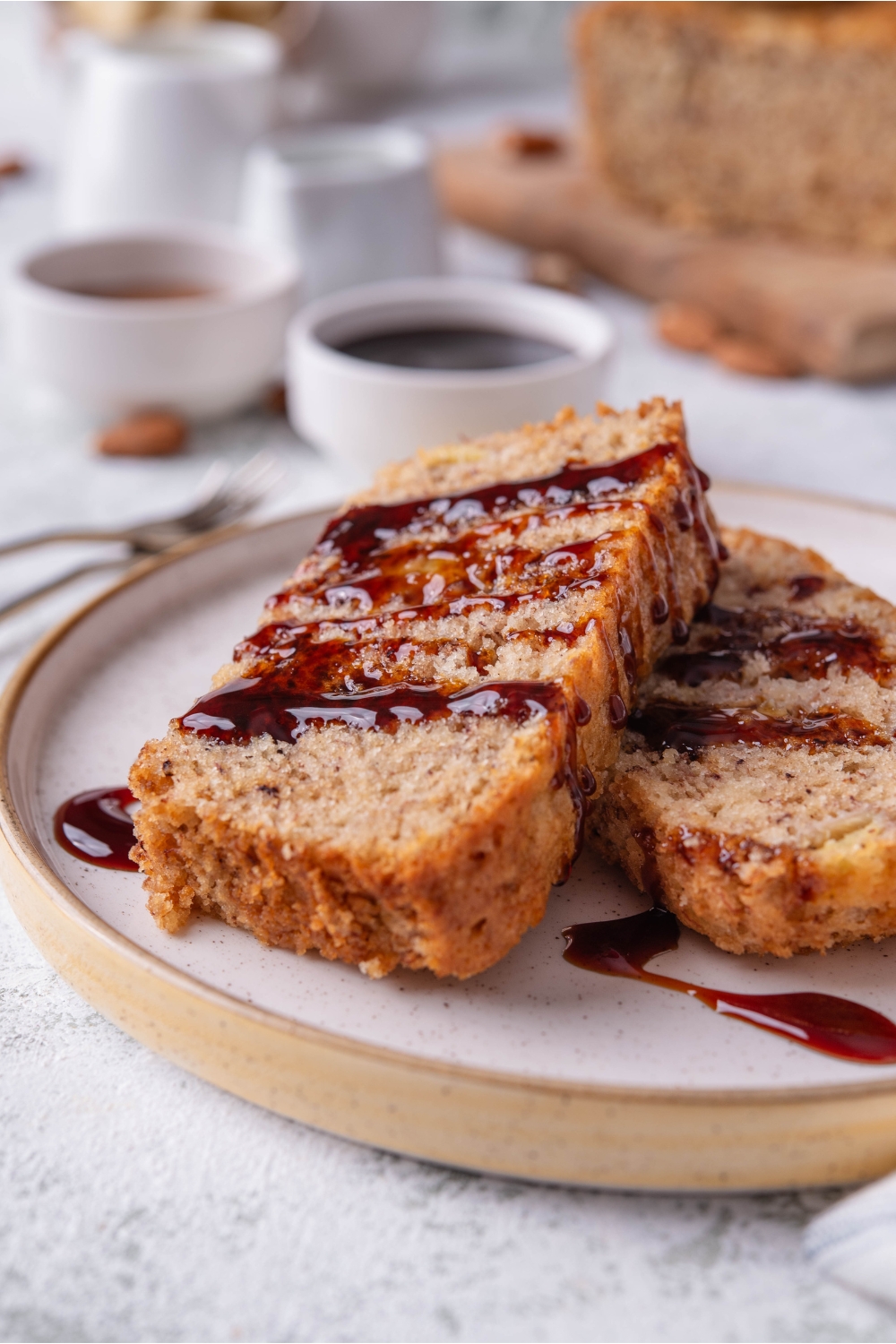 Two slices of banana bread overlapping each other on a plate, both with a drizzle of dark jam on top.