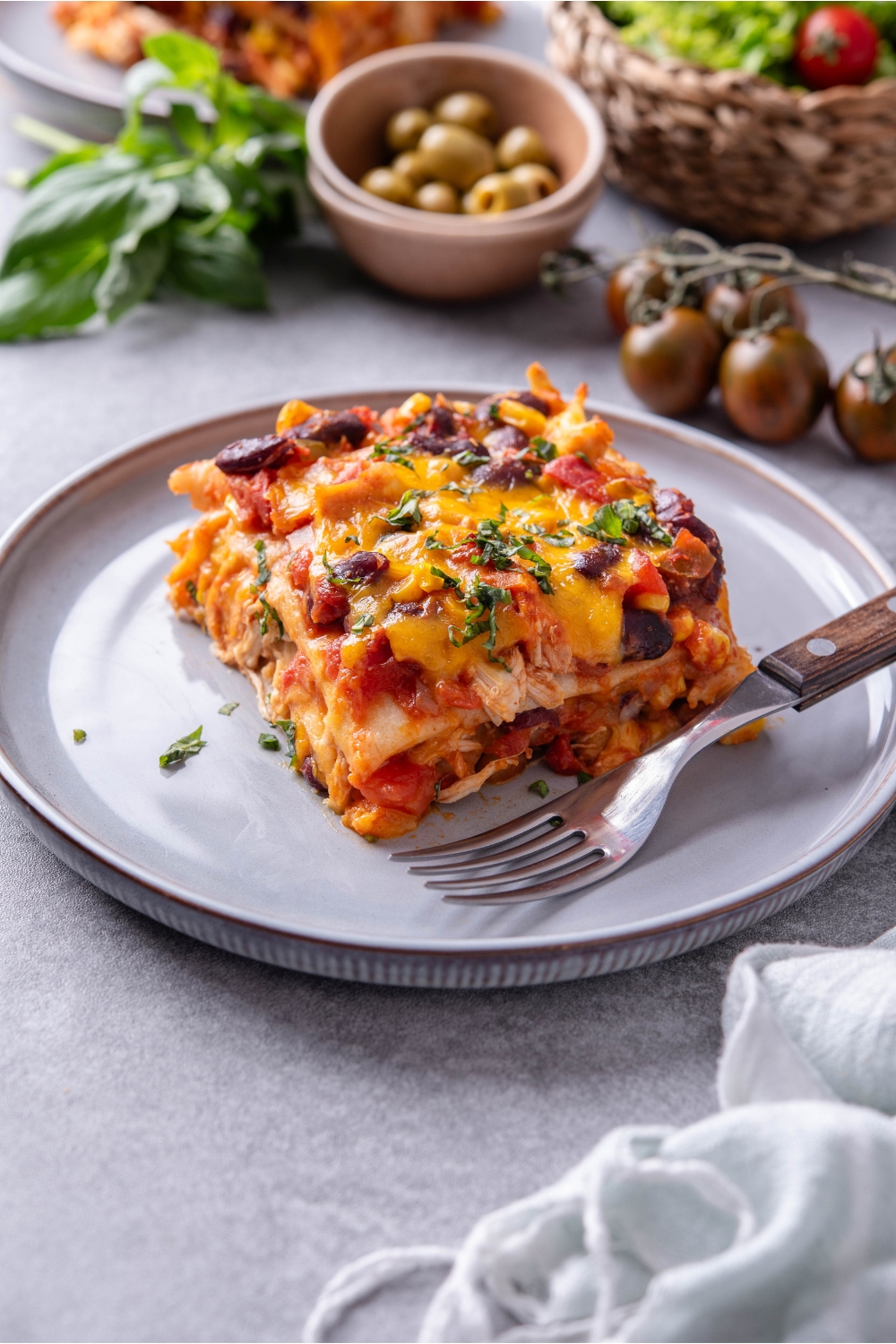 A square serving of chicken tortilla casserole layered with tomato sauce, shredded chicken, black beans, and topped with melted cheese, and fresh green herbs.