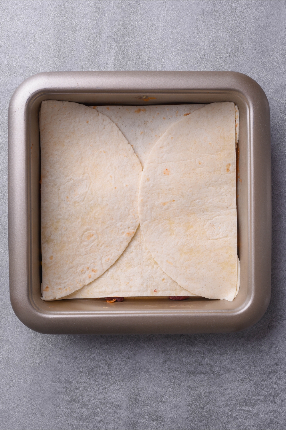 Square baking dish with a layer of tortillas that have been cut in half to fully cover the baking dish.