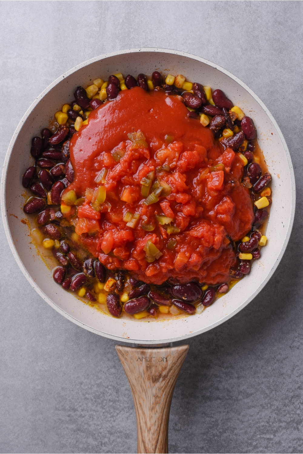 Grey skillet filled with black beans, corn, tomato sauce, and diced tomatoes with green chiles.