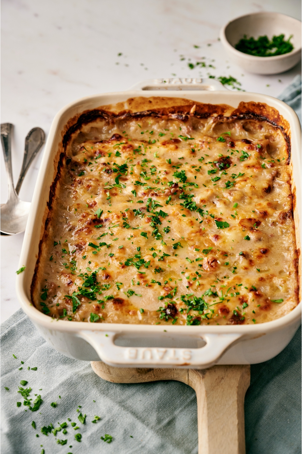 A white baking dish filled with freshly baked casserole covered in a layer of bubbly melted cheese and garnished with fresh green herbs.