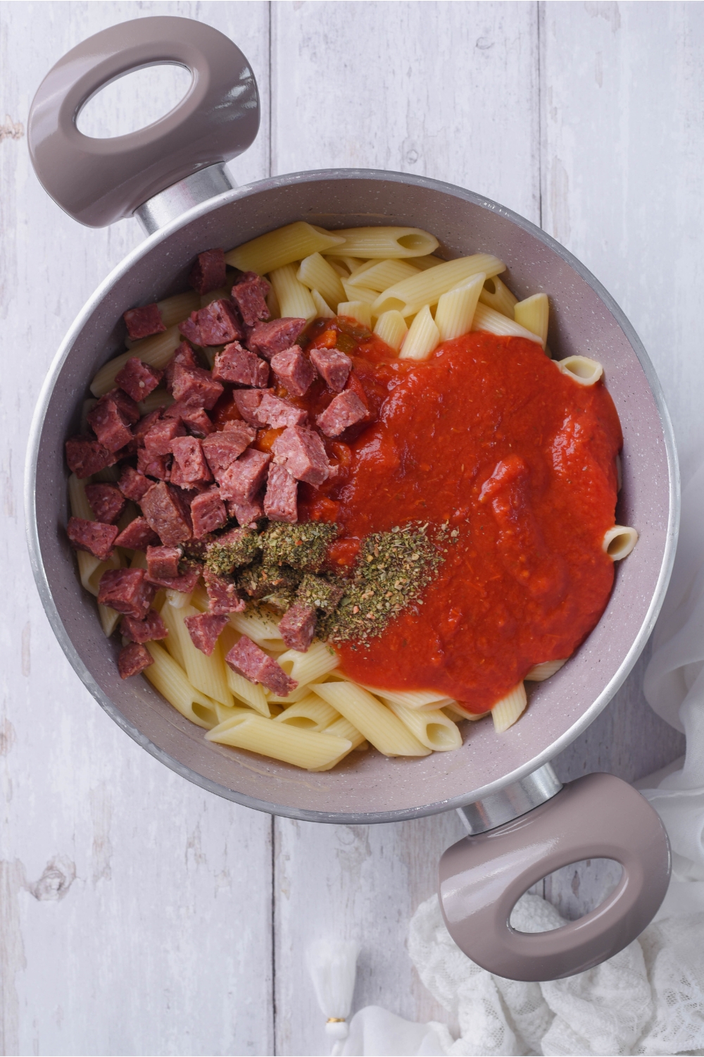 A grey pot filled with cooked penne pasta, red sauce, diced pepperoni, and spices that have been added but are not yet combined.