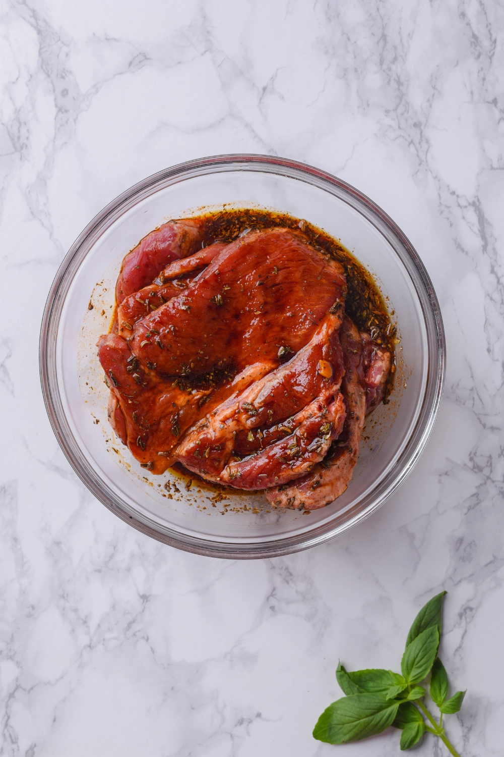 A clear bowl filled with raw pork steaks soaking in a brown marinade.