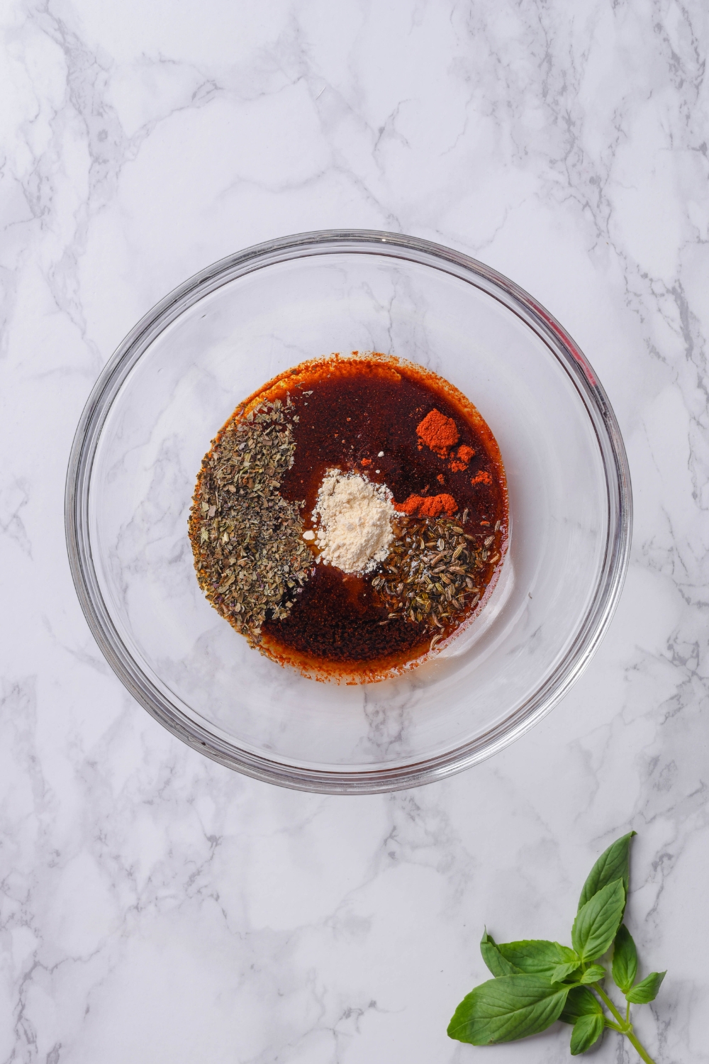 A clear bowl filled with soy sauce, spices, and dried herbs.