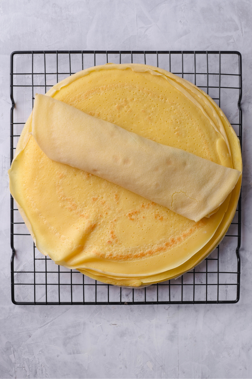 A wire rack with a stack of flat cooked crepes.