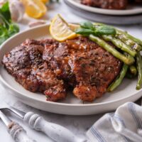 Two seasoned pork steaks layered on top of each other with a side of green beans and two lemon wedges.
