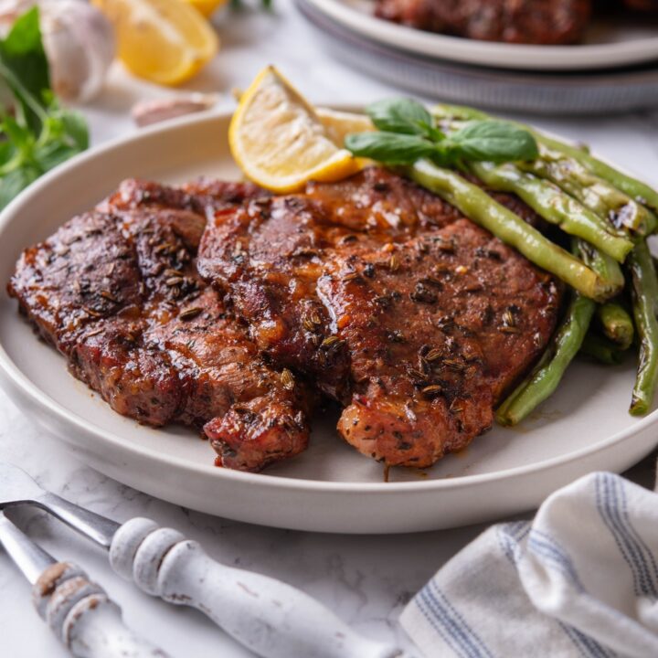Two seasoned pork steaks layered on top of each other with a side of green beans and two lemon wedges.