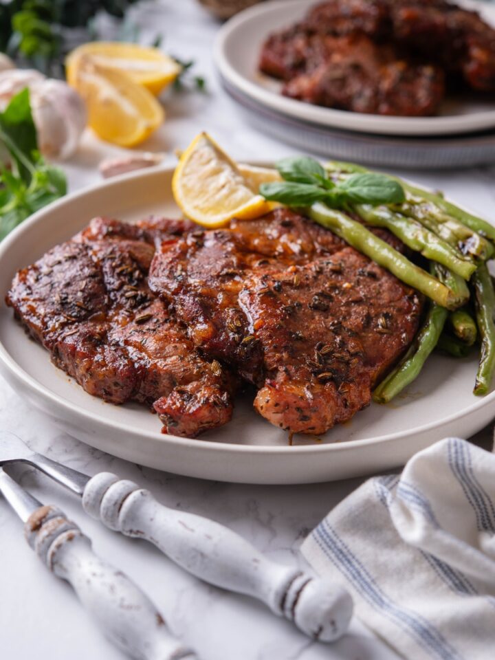Two seasoned pork steaks layered on top of each other with a side of green beans and two lemon wedges.