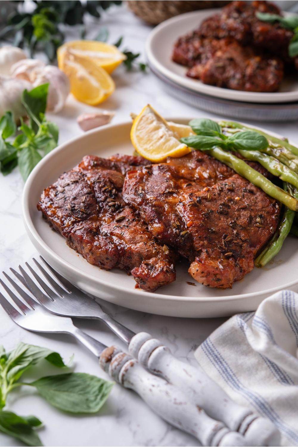 Two seasoned pork steaks layered on top of each other with a side of green beans and two lemon wedges. Two forks are next to the plate.