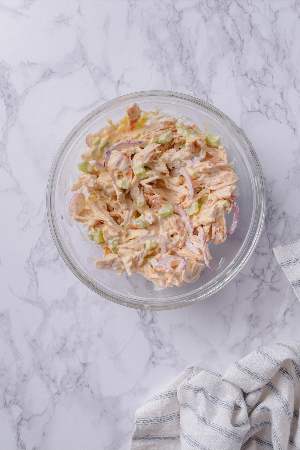 A clear bowl filled with chicken salad with visible pieces of diced celery and thinly sliced red onion.