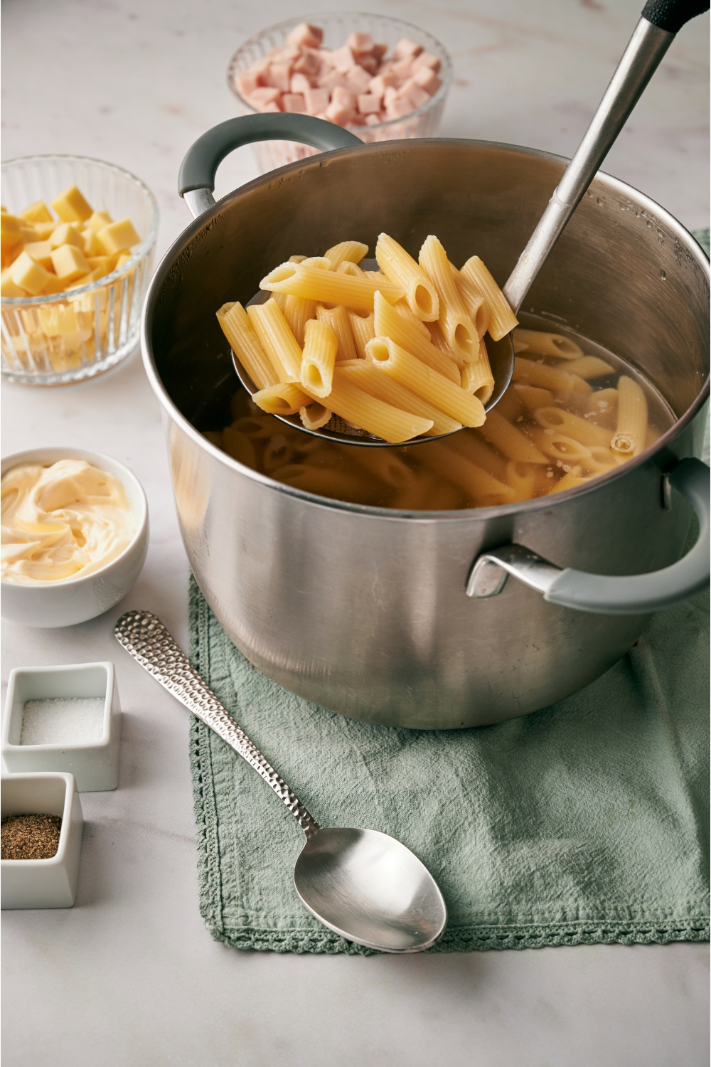 A pot of penne pasta cooking in water with a ladle of pasta being removed from the pot.