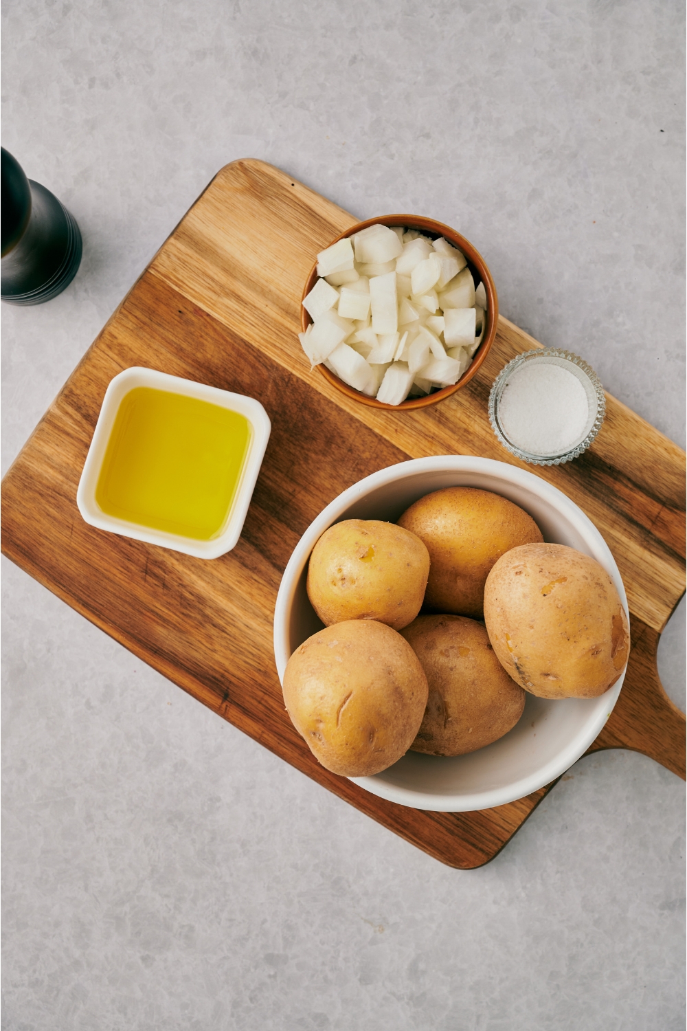 Bowls of potatoes, diced onion, salt, and oil on a wooden cutting board.