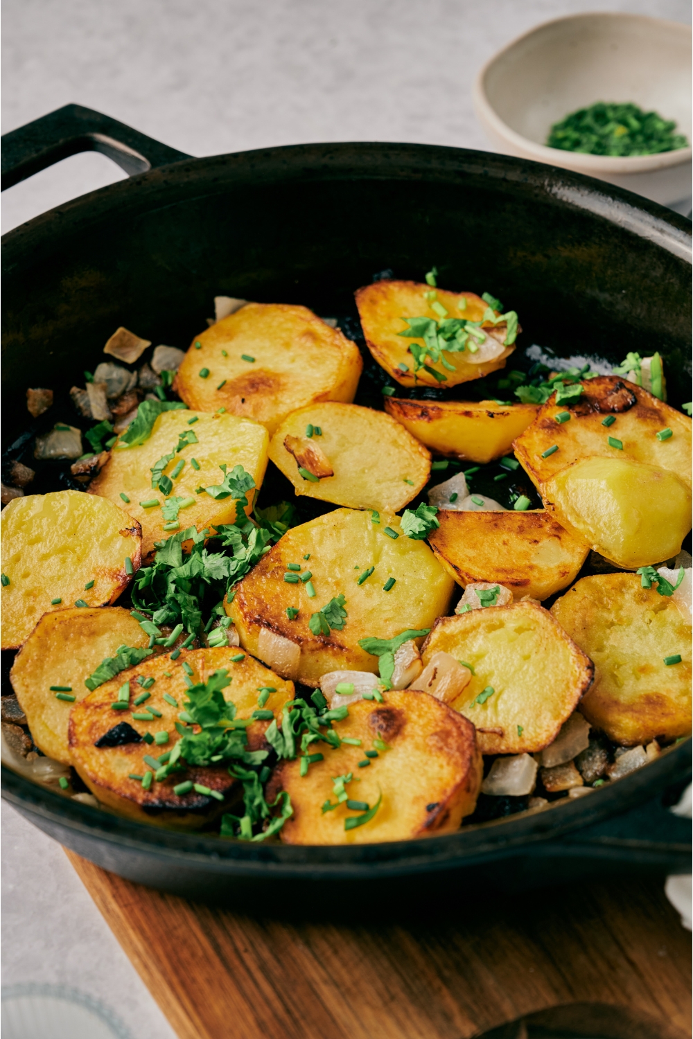 A skillet with pan fried potatoes and onions garnished with fresh green herbs.