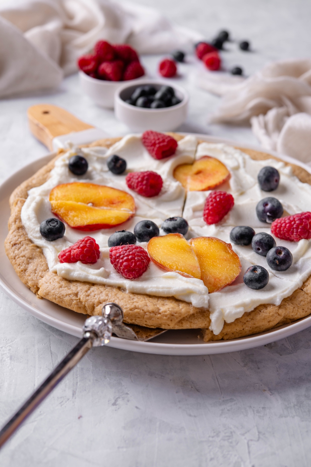A plate with fruit pizza sliced and ready to serve with a spatula underneath a slice.