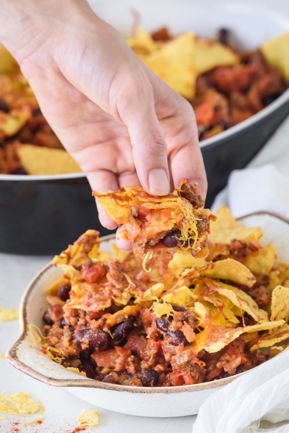 A bowl with taco casserole a hand is holding a chip piled with taco casserole on it.