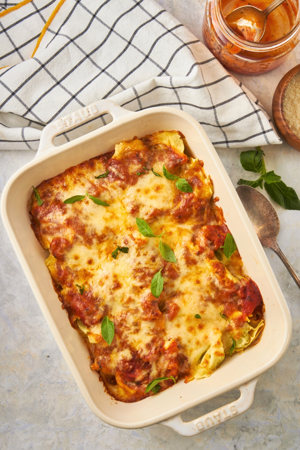 Basil leaves on top of cheesy baked tortellini in a white baking dish on top of a white counter.