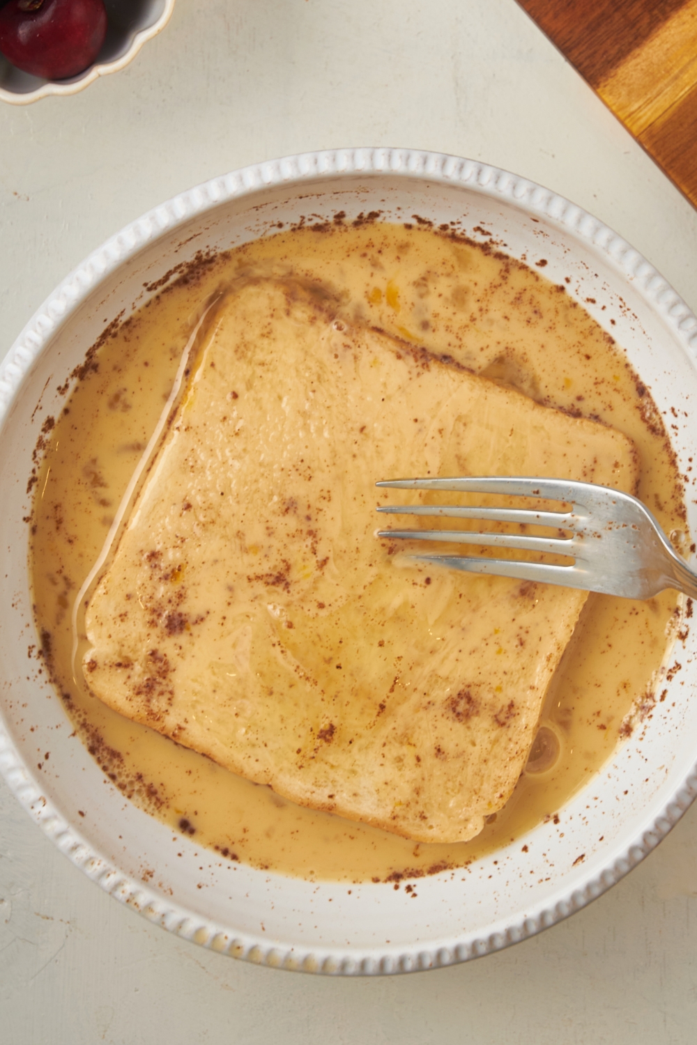 A mixing bowl with french toast egg mixture and a slice of bread being dipped in it with a fork.