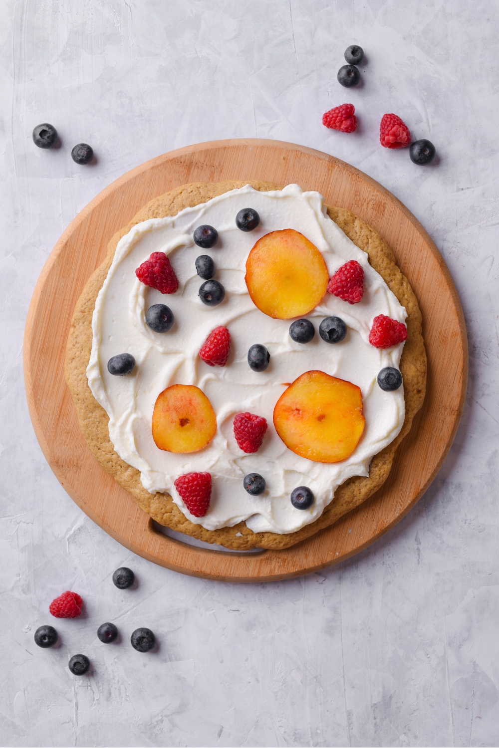 A wooden round board with an assembled fruit pizza.