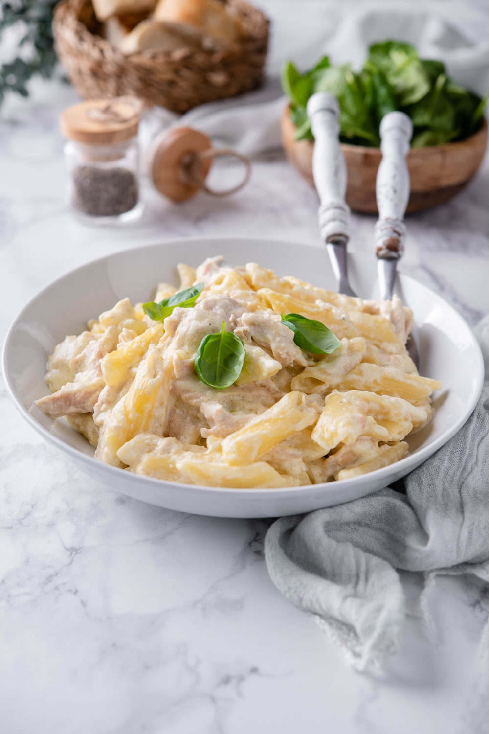 Chicken alfredo garnished with basil and served in a shallow bowl with two forks.