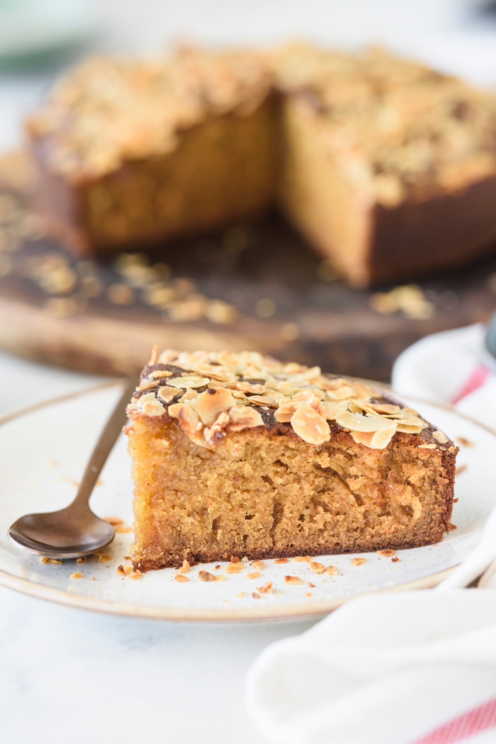 A slice of honey cake topped with sliced almonds on a plate with a spoon.