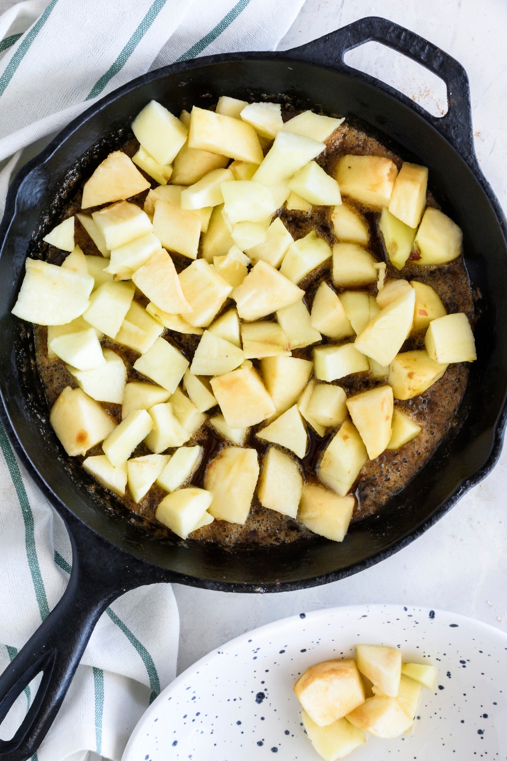 A cast iron skillet frying apples with a cinnamon sugar butter sauce.