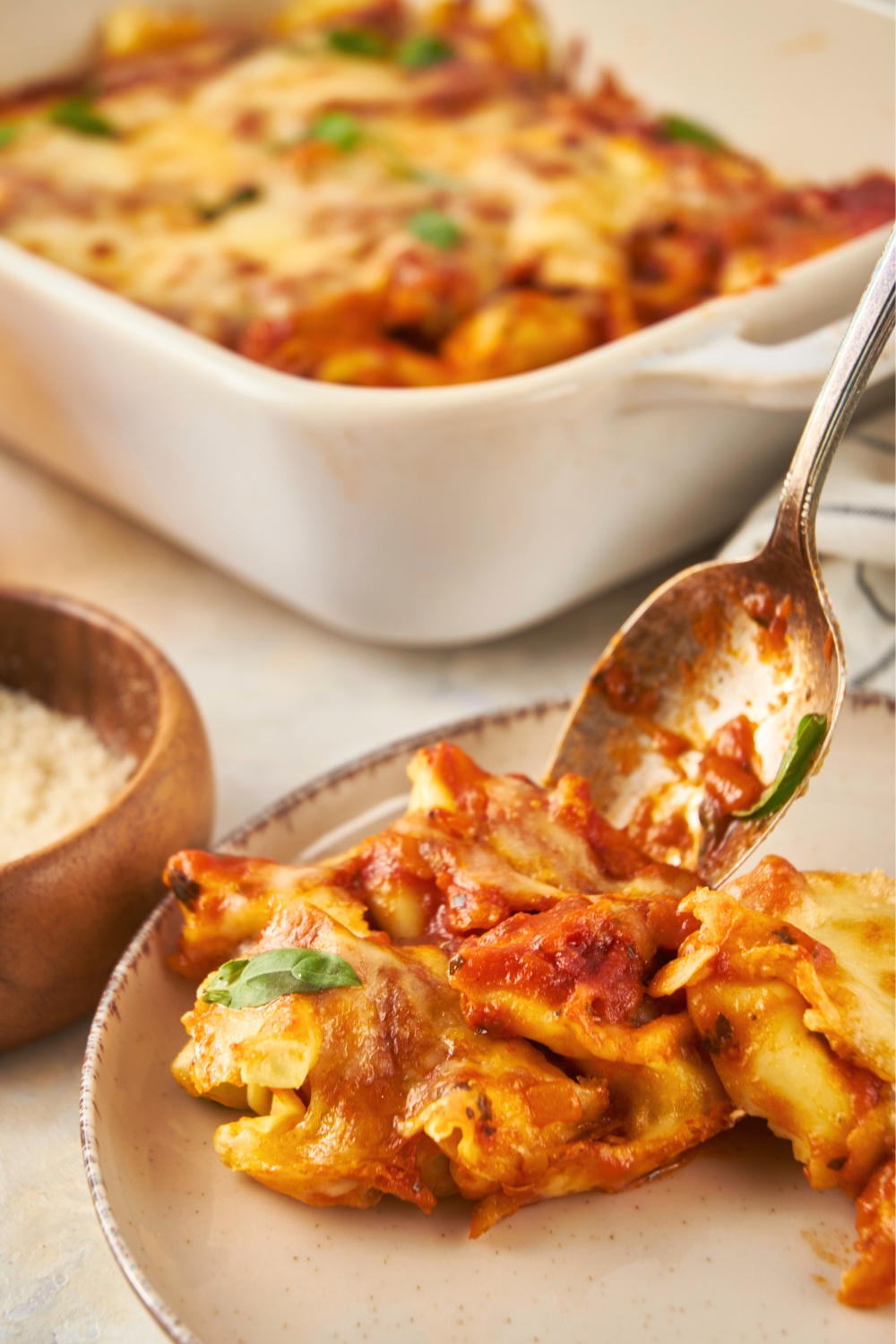 A spoon putting some baked tortellini on to part of a grey plate.