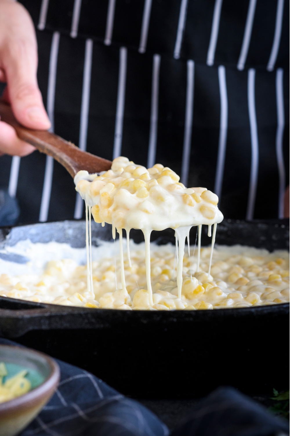 Cheesy cream cheese corn being scooped out of a cast iron skillet with a wooden spatula.