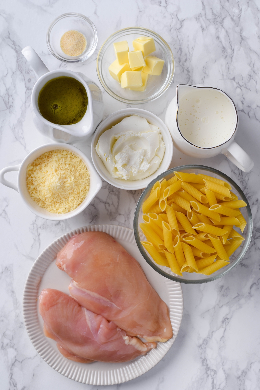 Raw chicken breasts, uncooked pasta, small bowls of cream, cheeses, chicken stock, butter, and garlic powder.