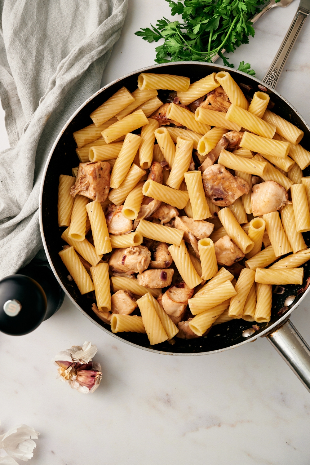A skillet with cooked pasta and chicken being added to sauce with mushrooms.