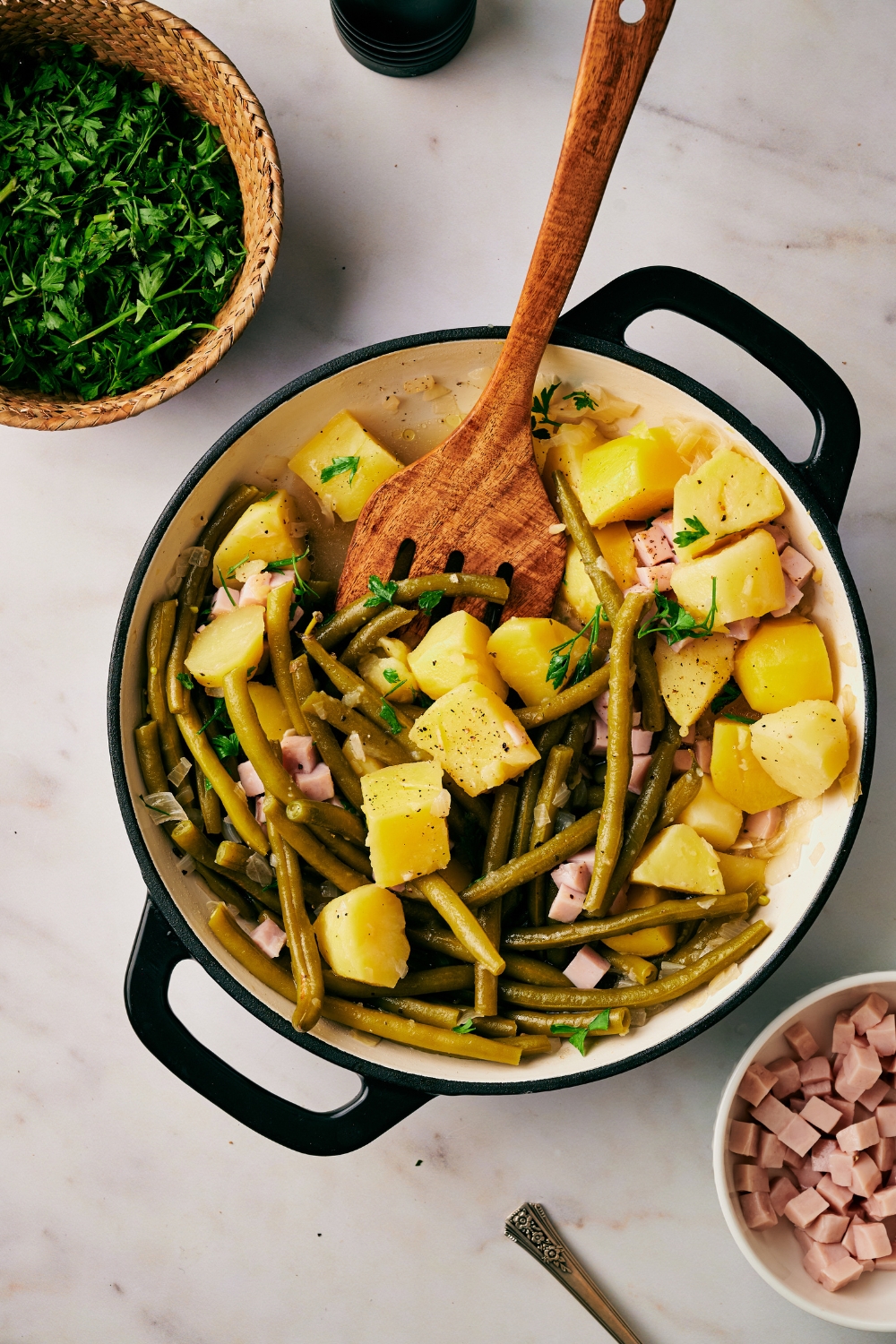A pot with ham, green beans, and diced potatoes. A wooden spatula is in it.