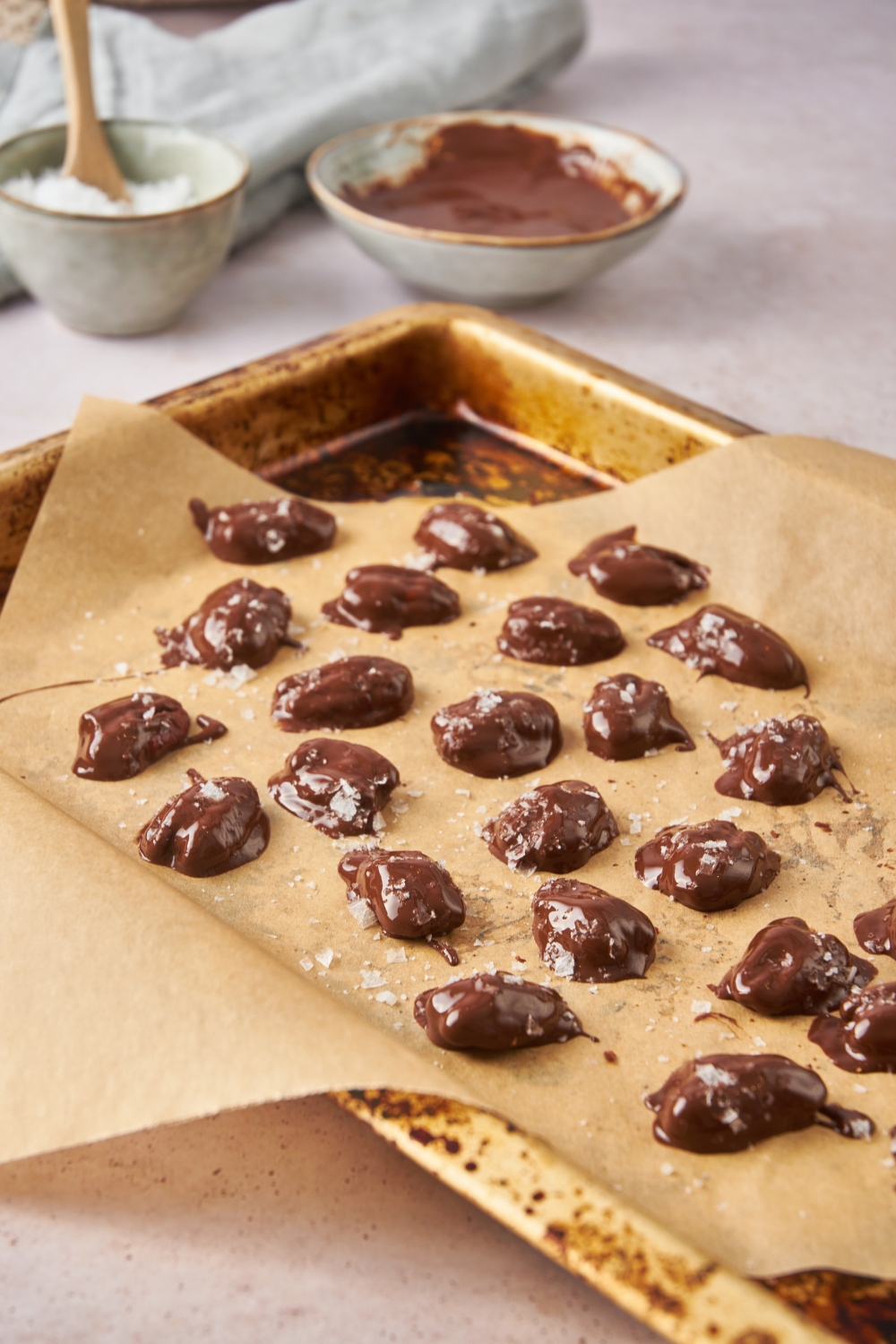 A baking sheet lined with parchment paper with chocolate covered pecans topped with salt.