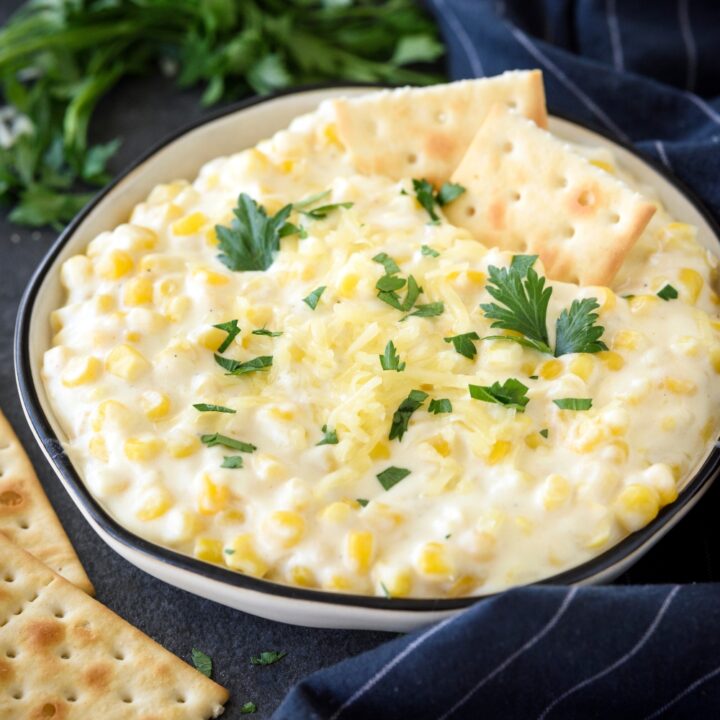 A closer look at cream cheese corn in a bowl, garnished with crackers and fresh parsley.