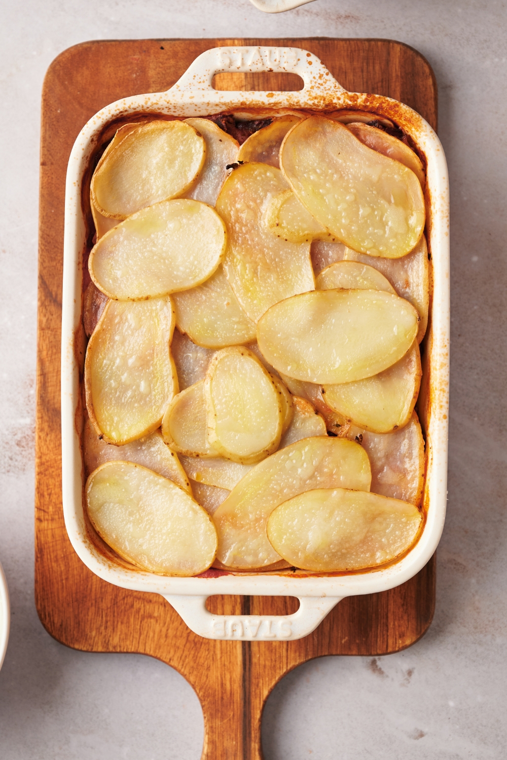 A casserole dish on a wooden serving board with baked shipwreck casserole without topping.
