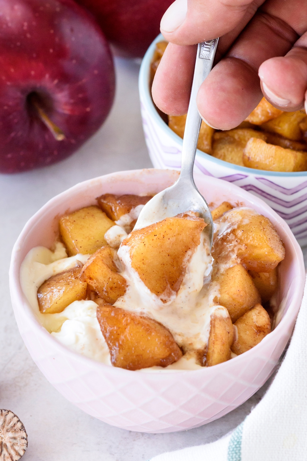 A small bowl of fried apples served on top of vanilla ice cream. A spoon is taking a scoop out of the bowl.