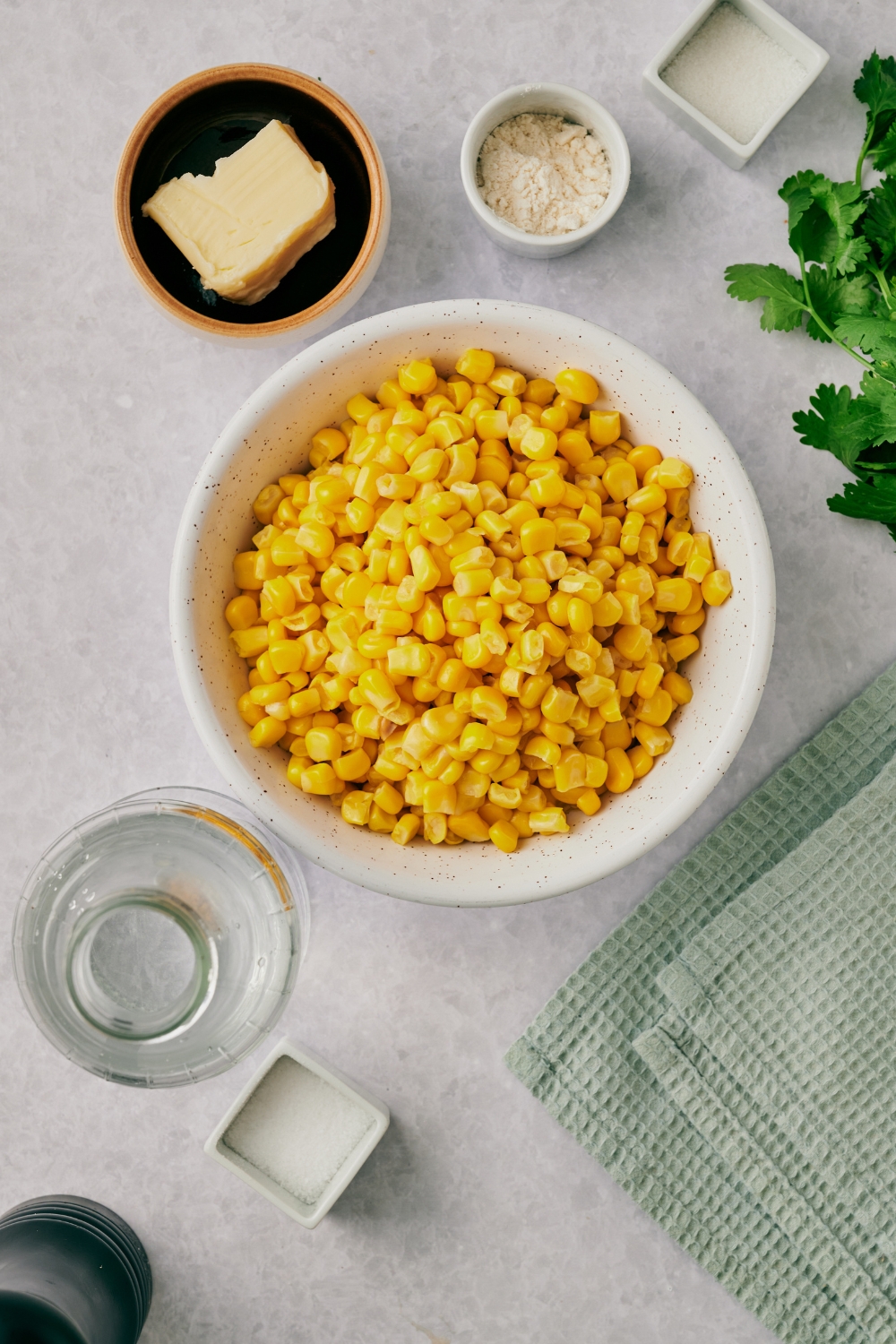 A countertop with multiple bowls containing corn, butter, sugar, flour, water, and salt and pepper.