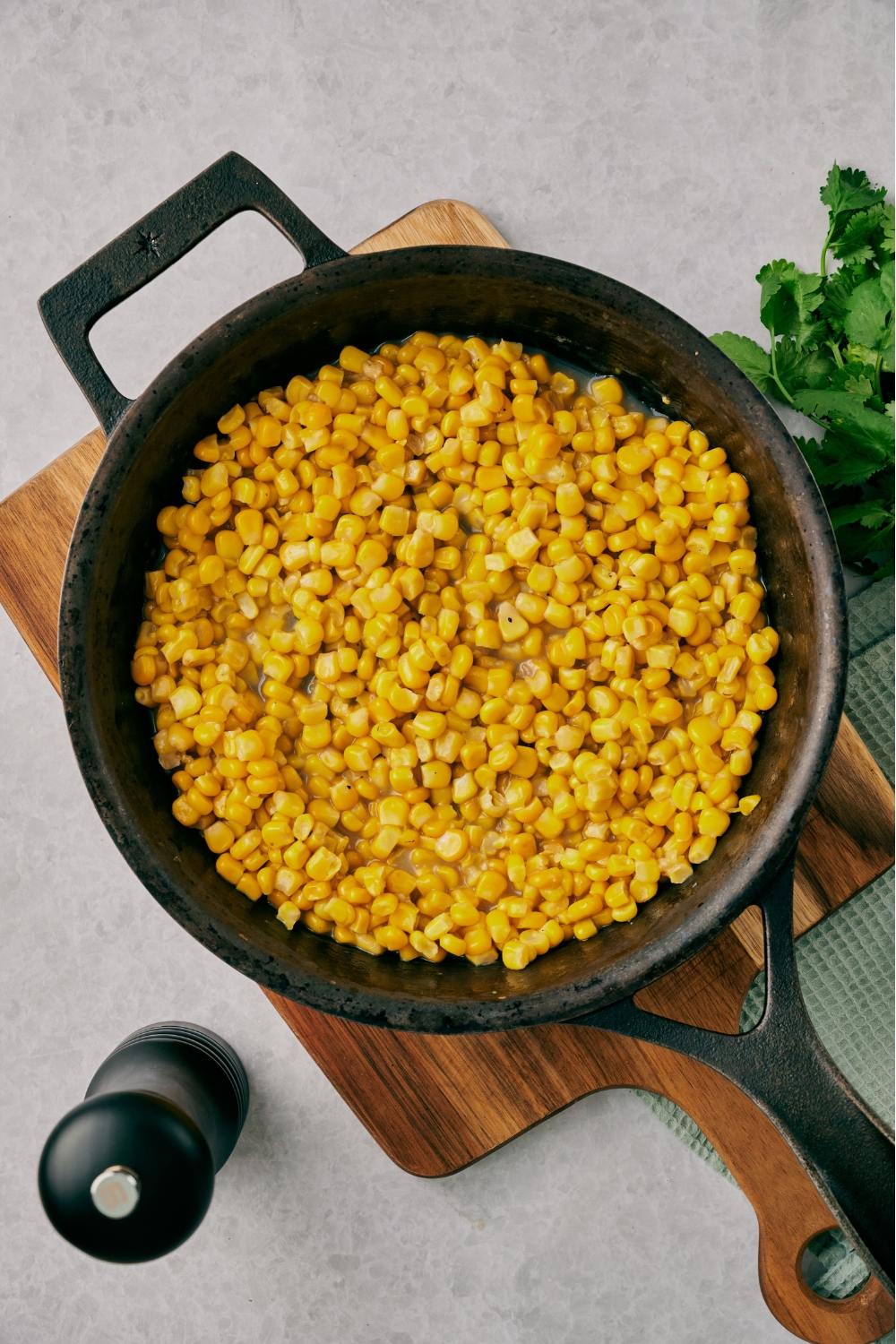 A cast iron skillet with fried corn sitting on a wooden serving board.