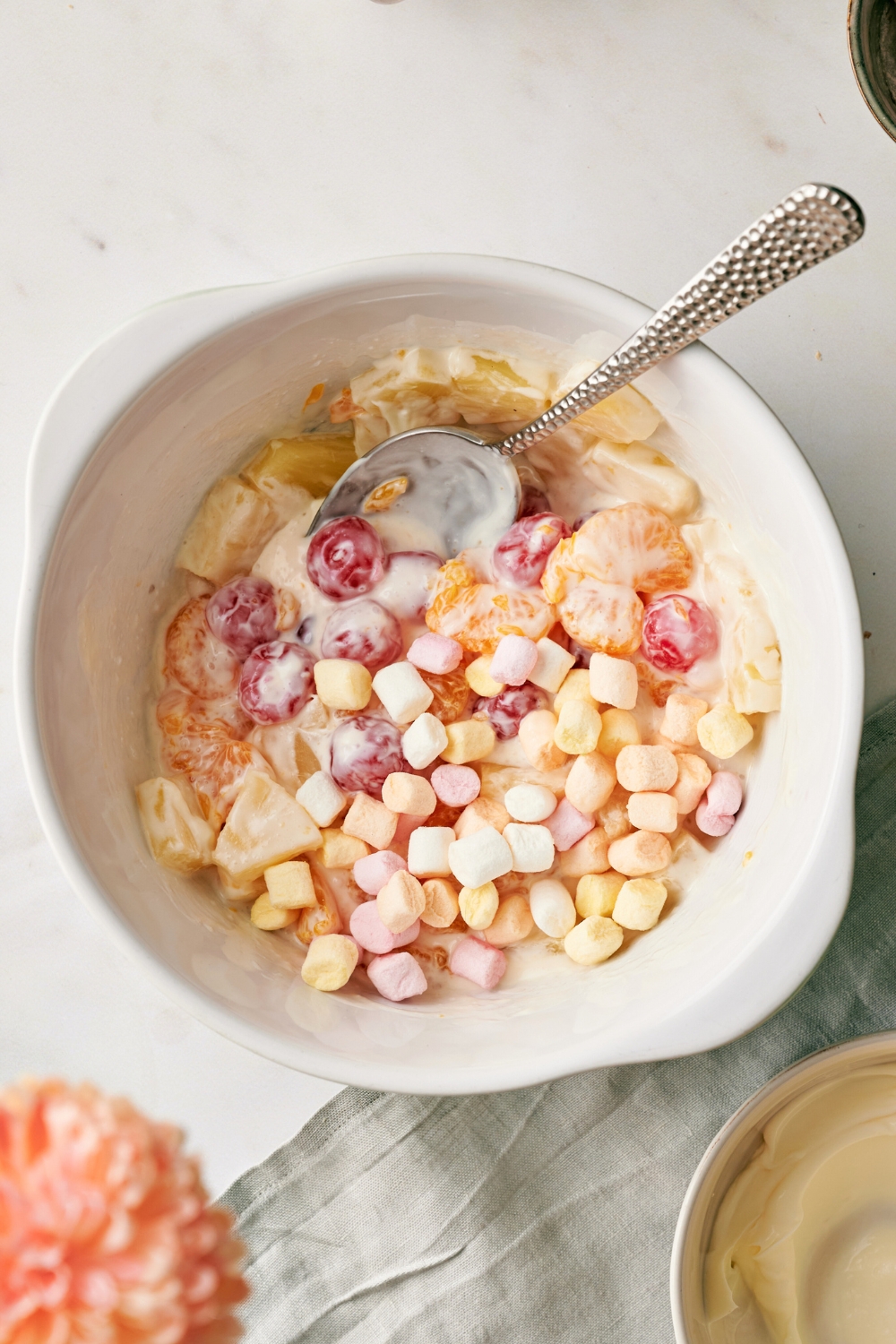A spoon in a bowl with mini marshmallows on top of a fruit salad mixture.