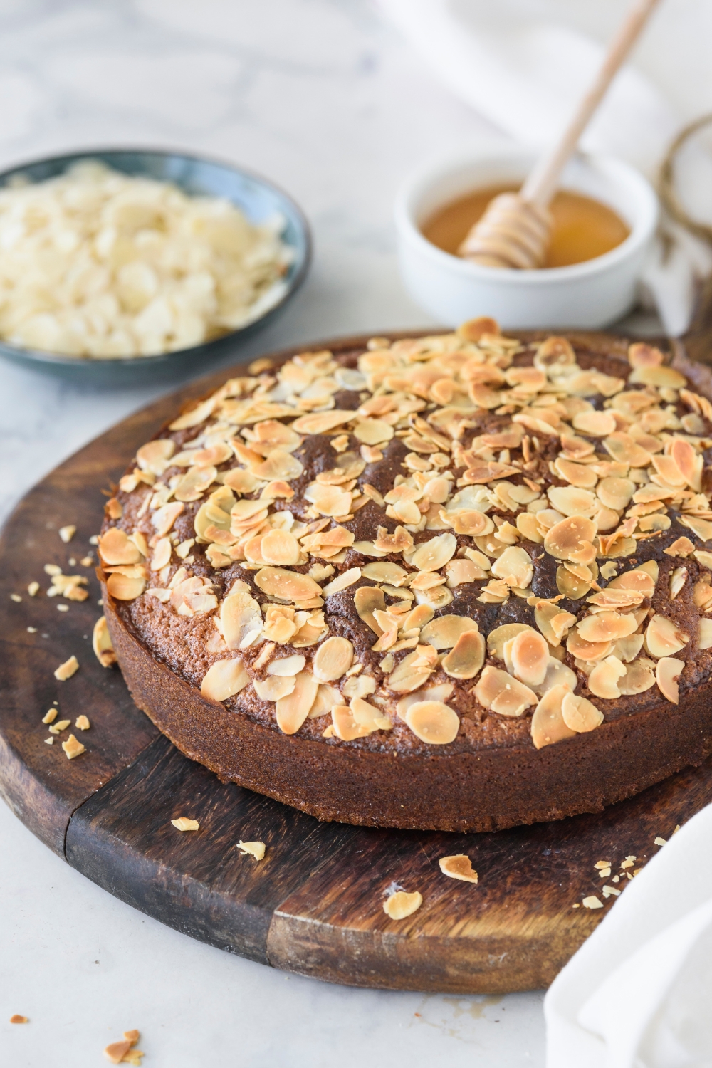 Honey cake topped with sliced almonds and served on a round wooden board.