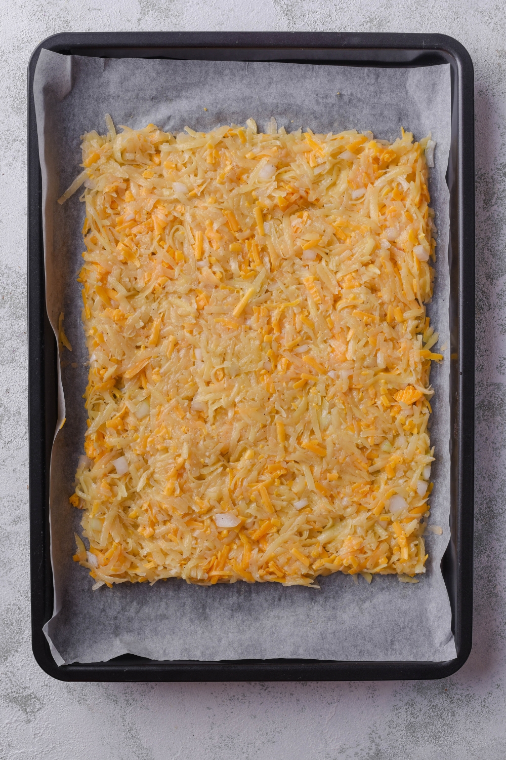 A baking sheet lined with parchment paper with condensed hash browns and cheese on it.