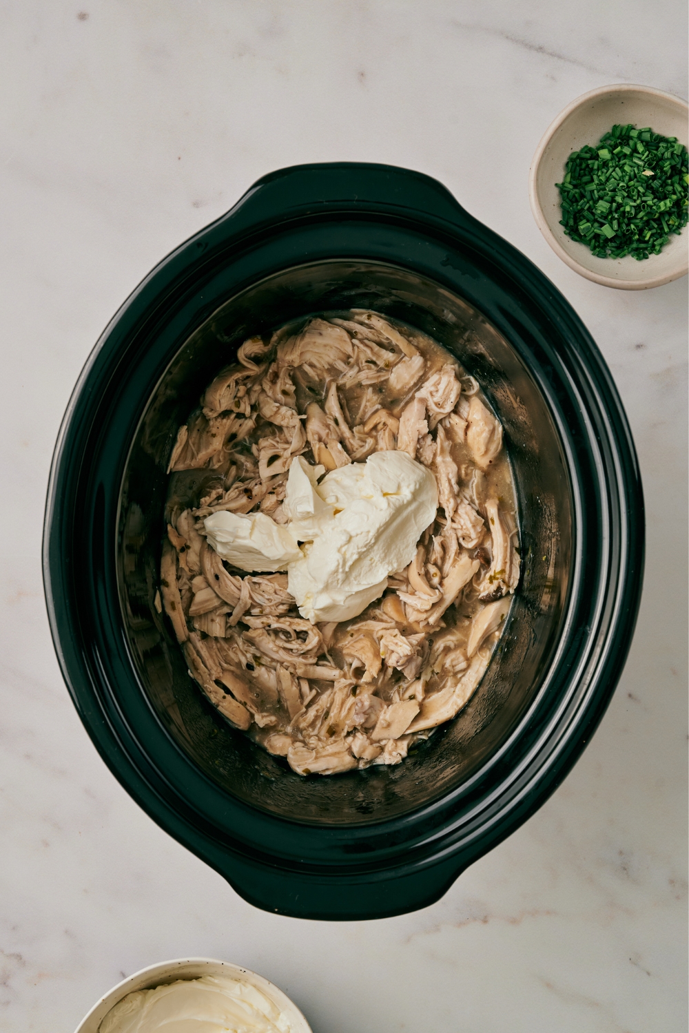 A crock pot with shredded chicken and cream cheese being added.