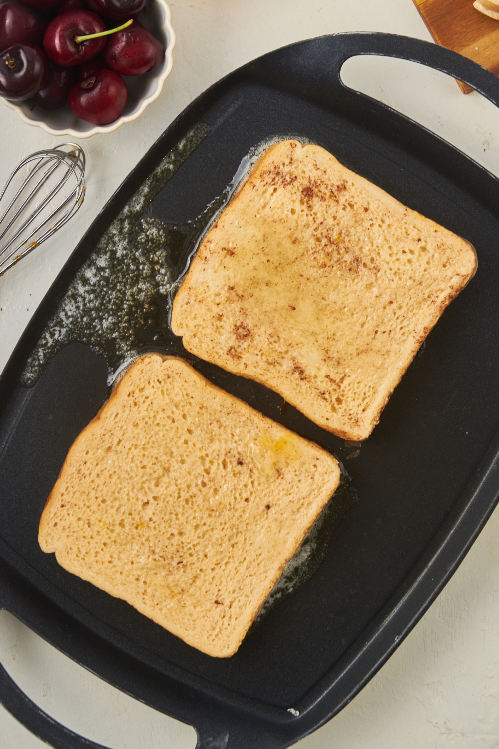 A griddle with two slices of french toast cooking.