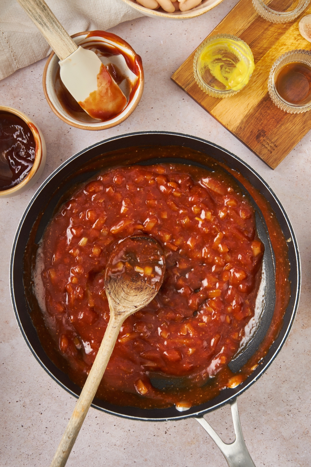 A wooden spoon in a skillet with a homemade sauce for baked beans.