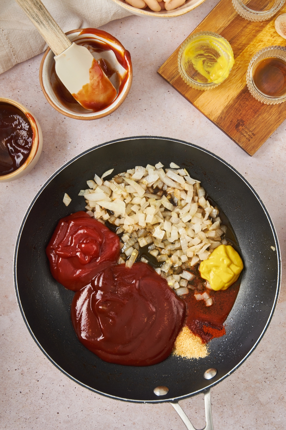 BBQ sauce, ketchup, sauteed onion, mustard, and spices in a skillet.