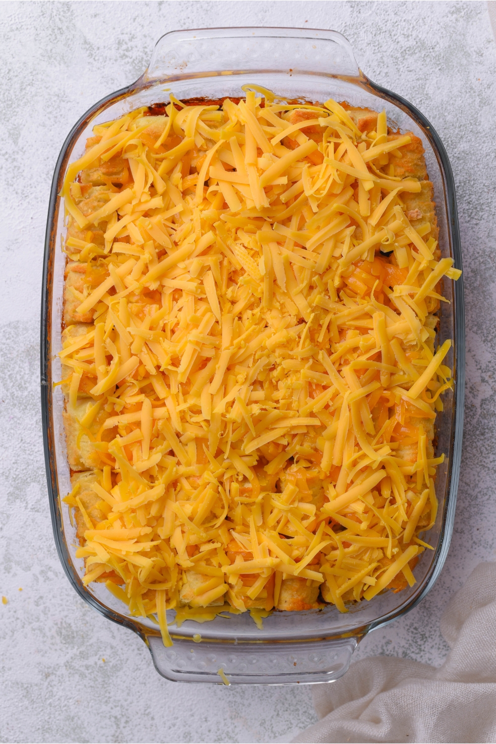 Shredded cheddar cheese on top of a Mexican tater tot casserole in a baking dish on a grey counter.